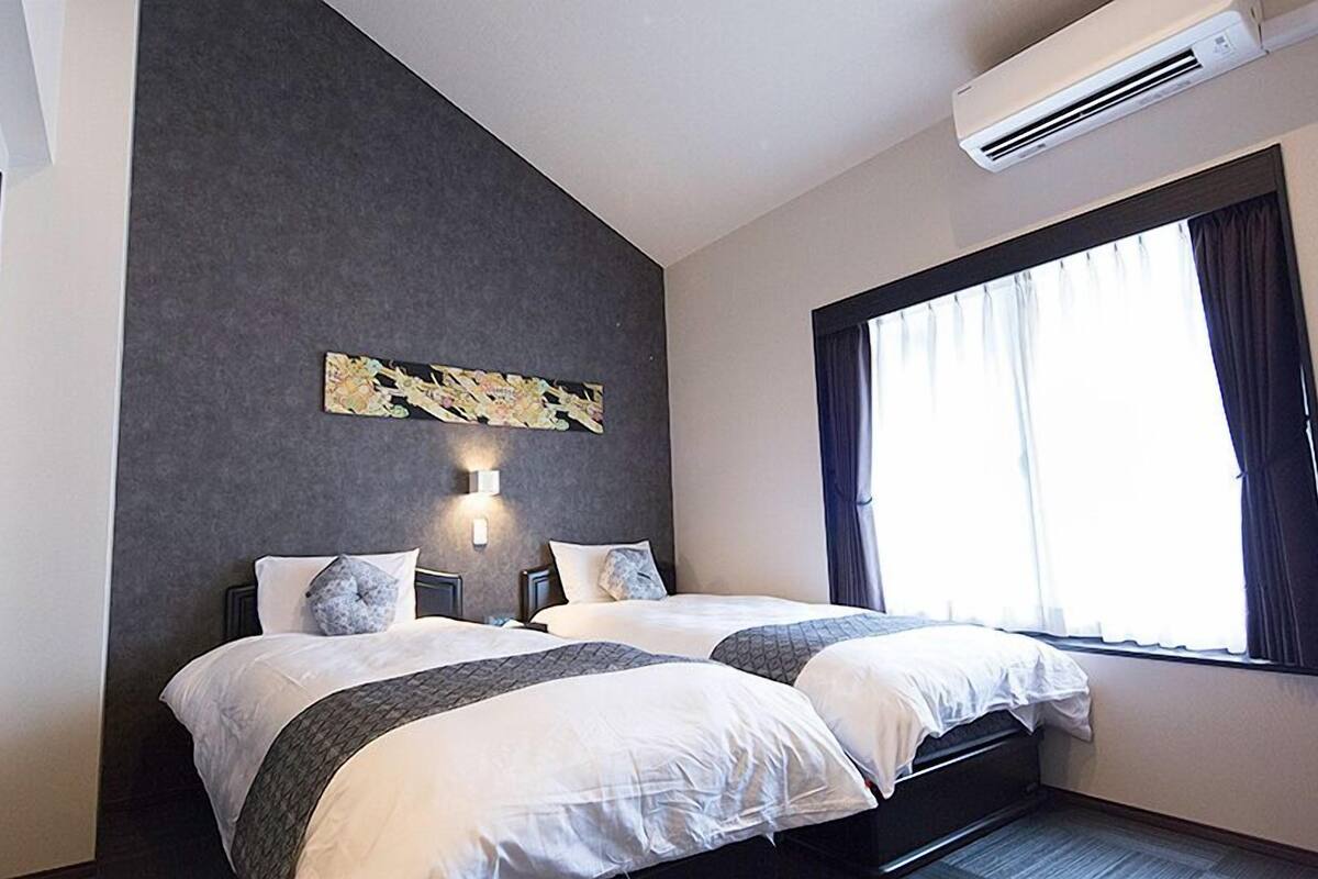Une chambre d’hôtel avec deux lits, une grande fenêtre avec des rideaux, un appareil de climatisation et une œuvre d’art accrochée au mur.
