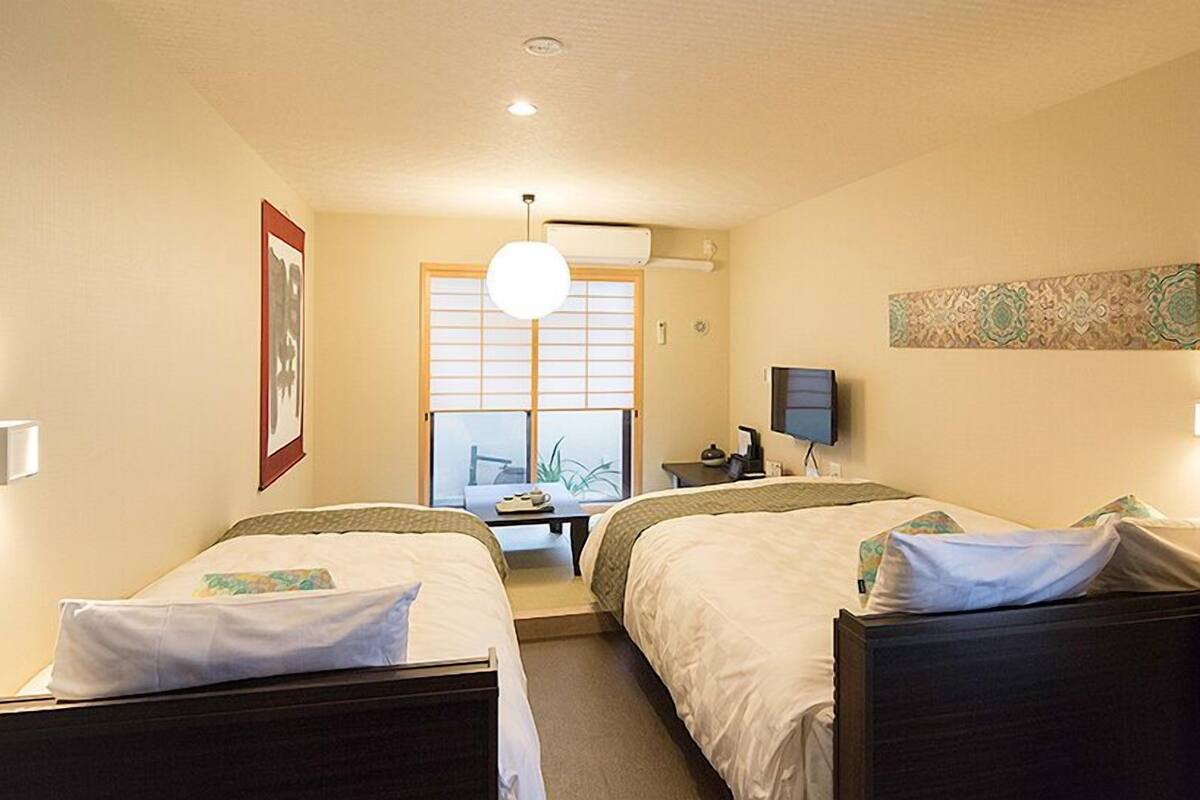 Une chambre d’hôtel avec deux lits, un bureau, une chaise, une télévision et une fenêtre donnant sur un beau paysage.