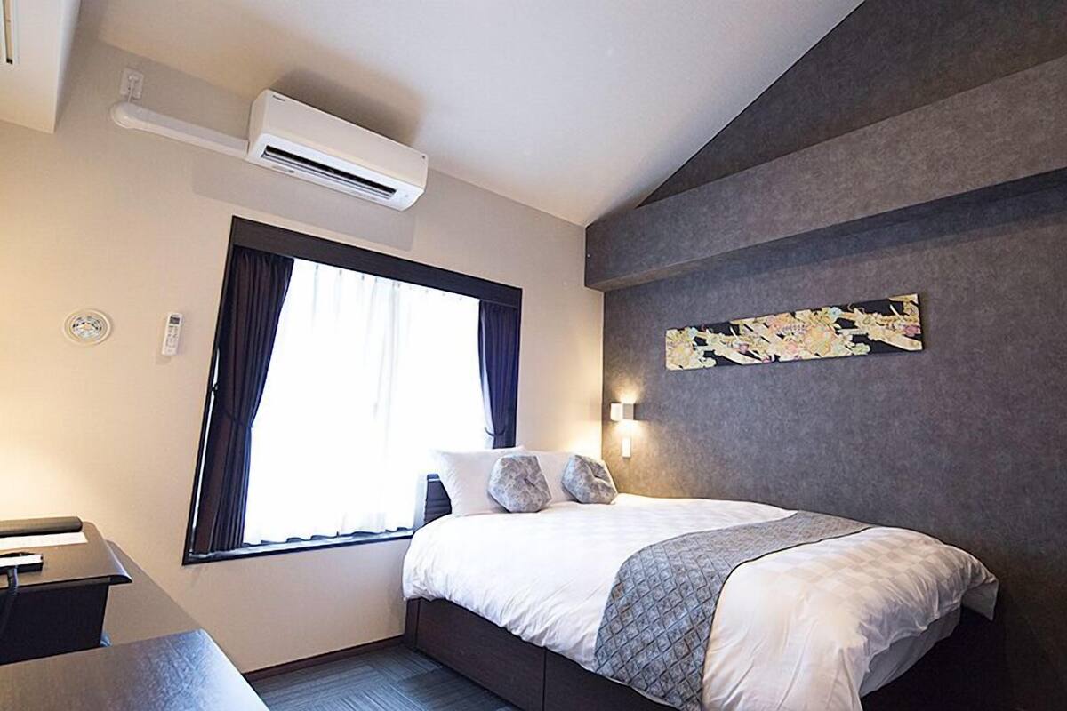 Une chambre d’hôtel moderne équipée d’un lit, d’une fenêtre, d’un climatiseur, d’une table de chevet et d’une œuvre d’art accrochée au mur.