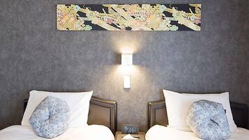 A hotel room with two beds, each with a patterned pillow, a nightstand with a clock, and a wall-mounted light fixture.