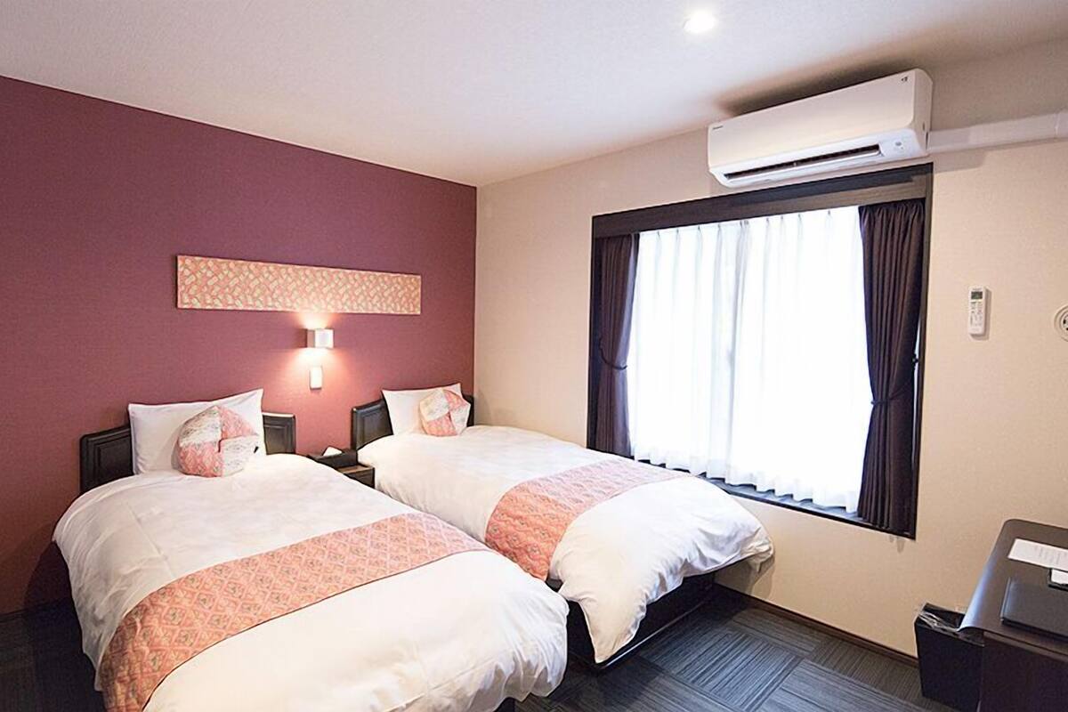 Une chambre d’hôtel avec deux lits, un climatiseur fixé au mur, une fenêtre avec des rideaux et un luminaire fixé au mur.