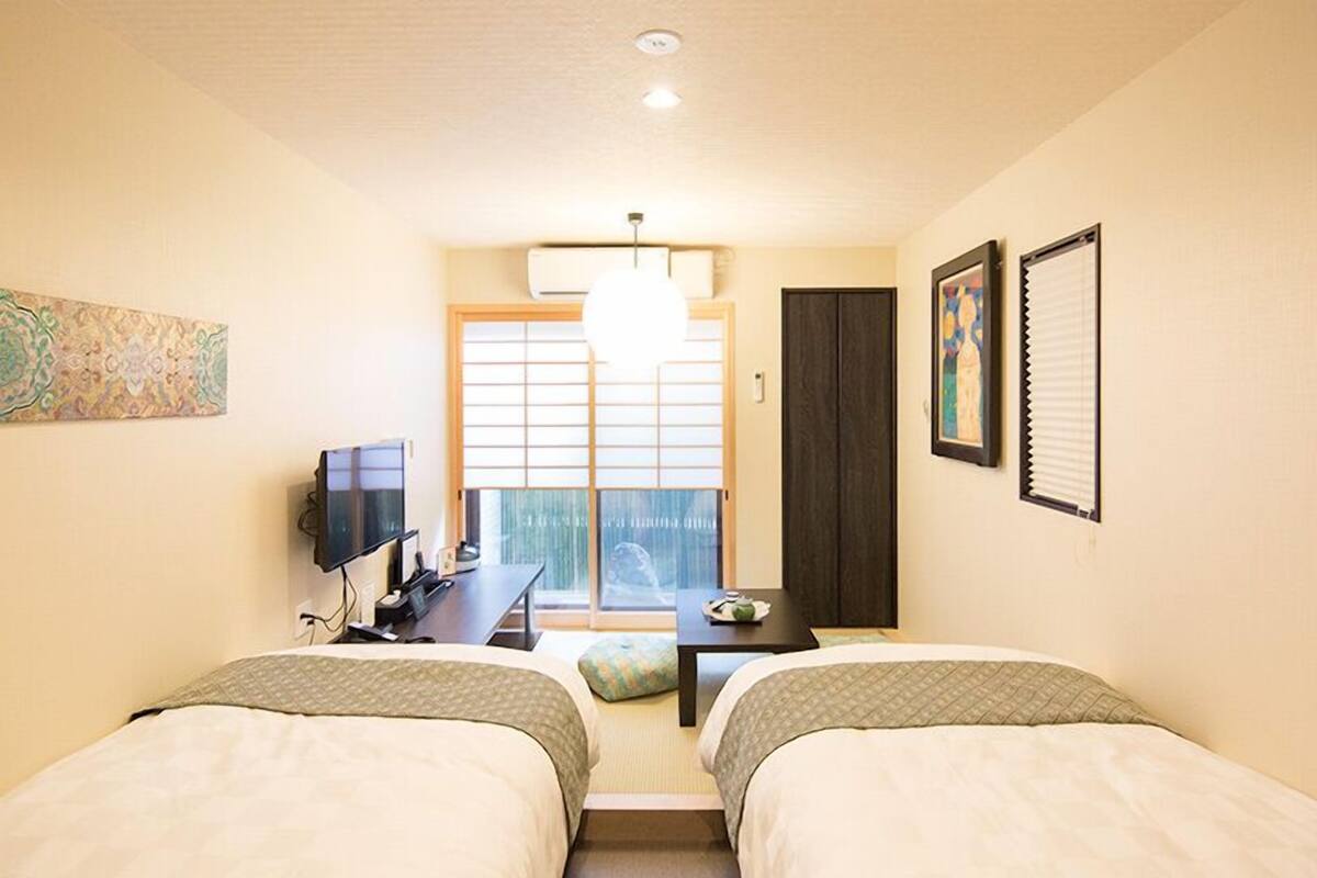 Une chambre d’hôtel avec deux lits, un bureau avec une télévision, une fenêtre donnant sur un beau paysage et des œuvres d’art accrochées aux murs.