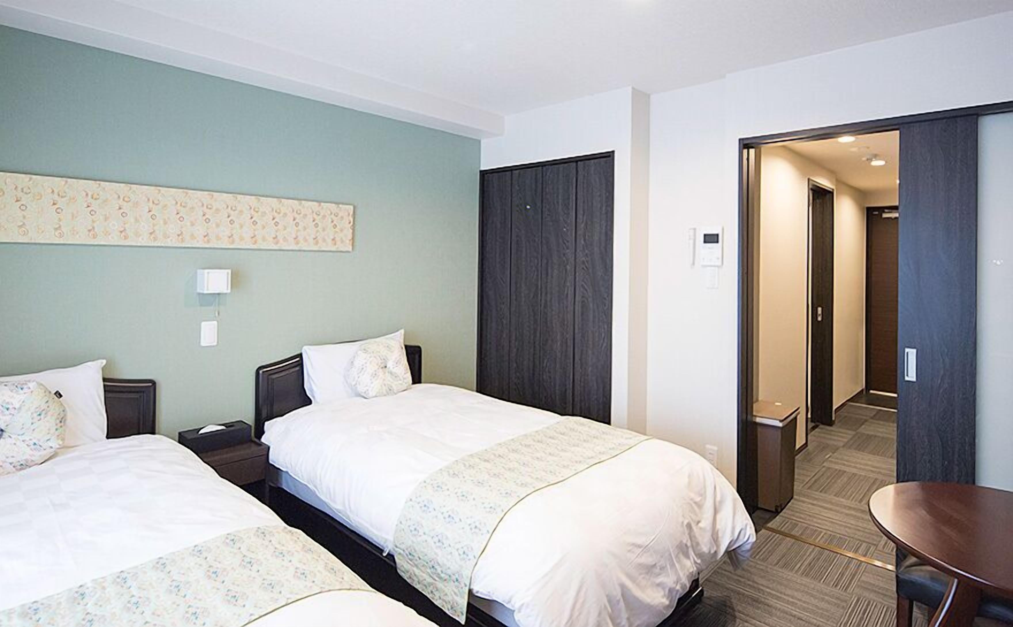 A hotel room with two beds, a desk, a wardrobe, and a bathroom visible through an open door.