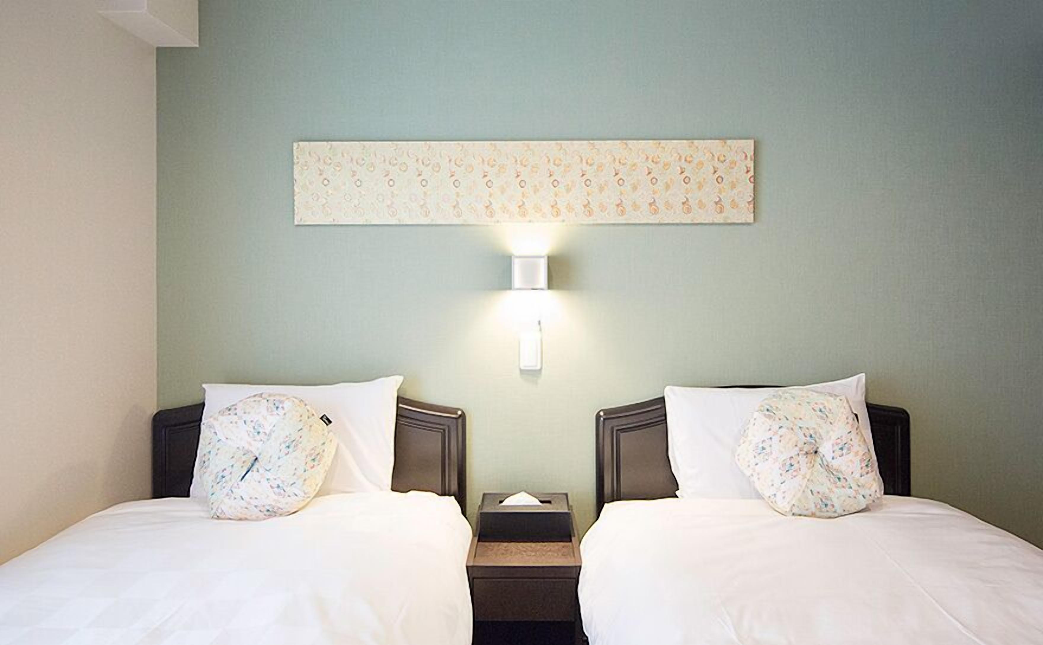 A hotel room with two beds, a nightstand, a wall-mounted light, and a decorative panel above the beds.