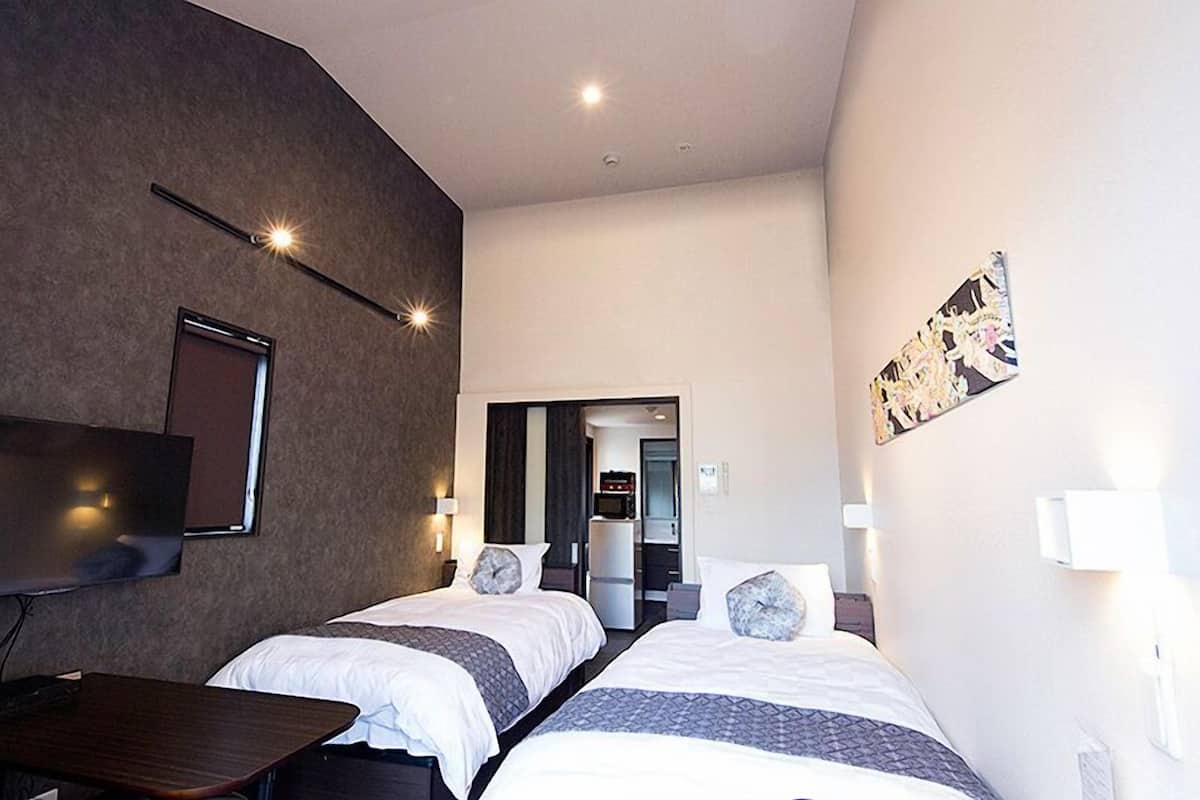 Une chambre d’hôtel avec deux lits, un bureau, un téléviseur à écran plat et une petite kitchenette.