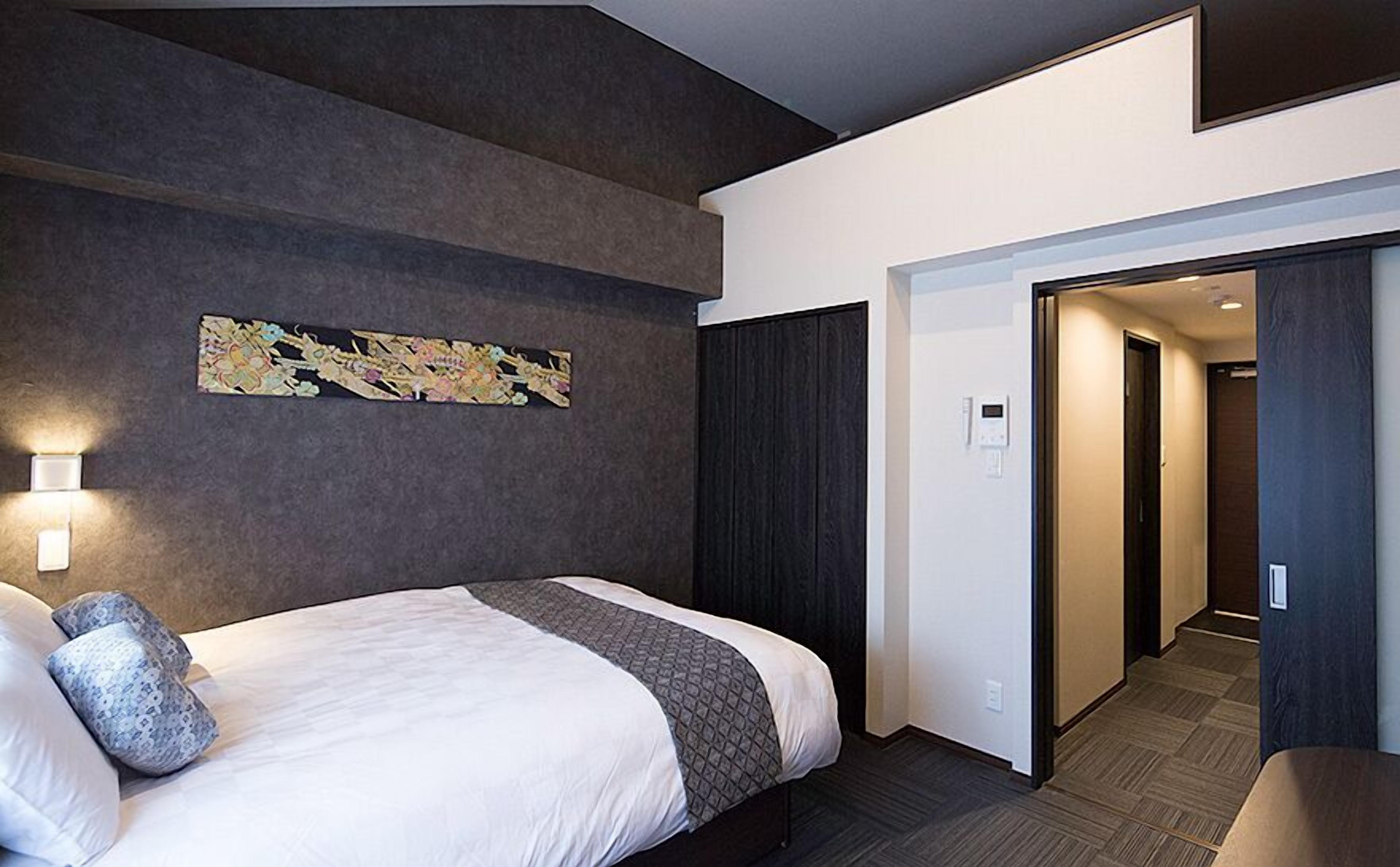 A modern hotel room with a large bed, a wall-mounted artwork, and a hallway leading to another room.