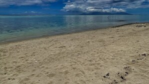 Ein Strand mit klarem Wasser, sandigem Ufer und bewölktem Himmel.