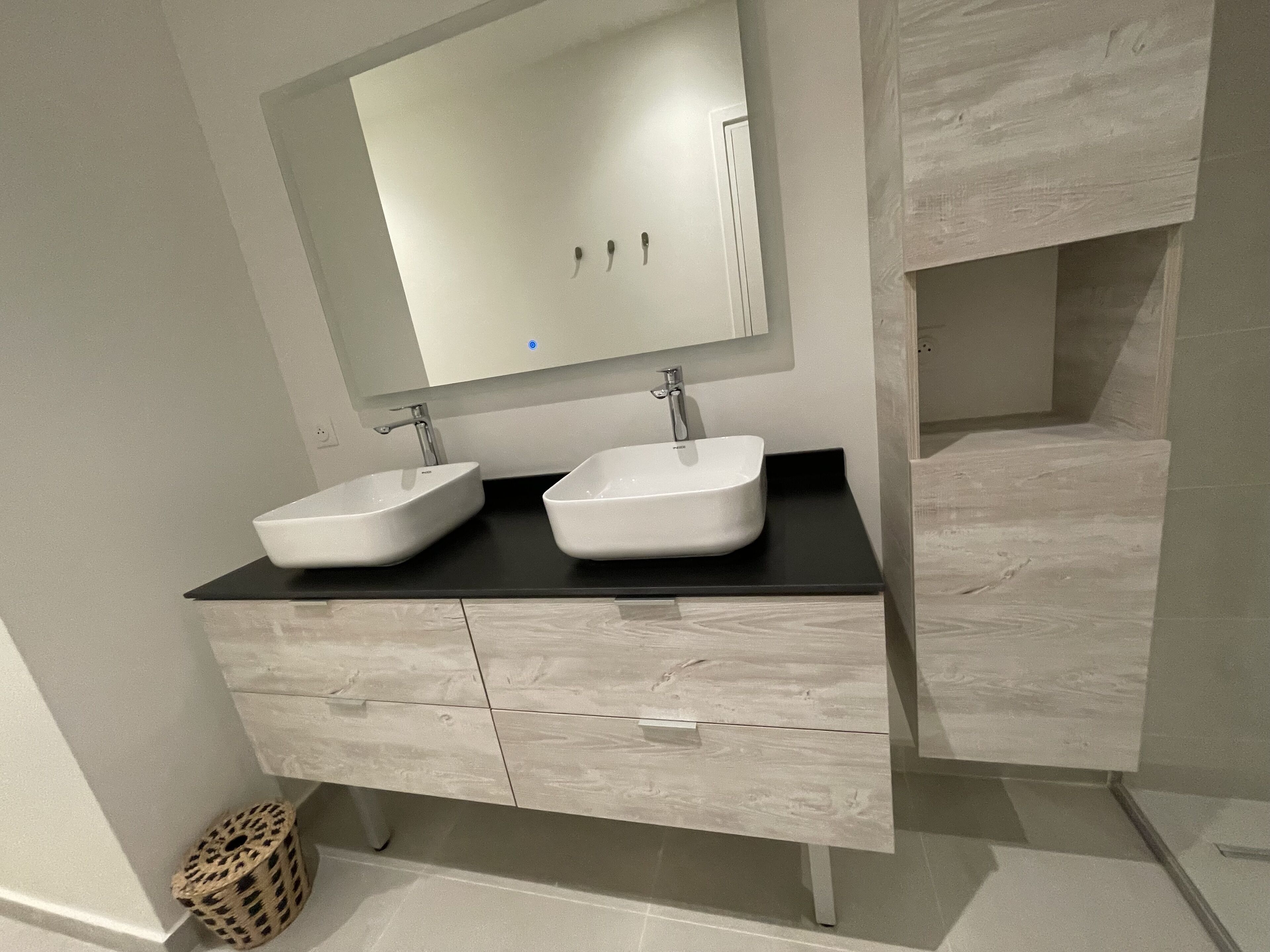 A bathroom with two white sinks, a black countertop, and a light wood vanity with drawers.