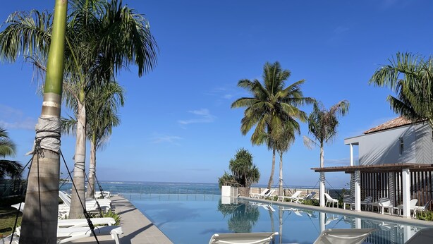 Ein Poolbereich mit Liegestühlen, Palmen und Blick auf den Ozean.