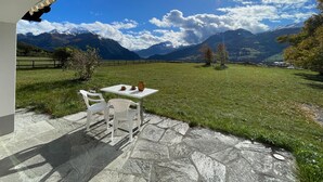 Une terrasse avec une table et des chaises donnant sur un champ verdoyant et des montagnes.
