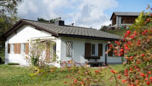 Une maison blanche avec un toit en pente, des volets en bois et une cheminée.