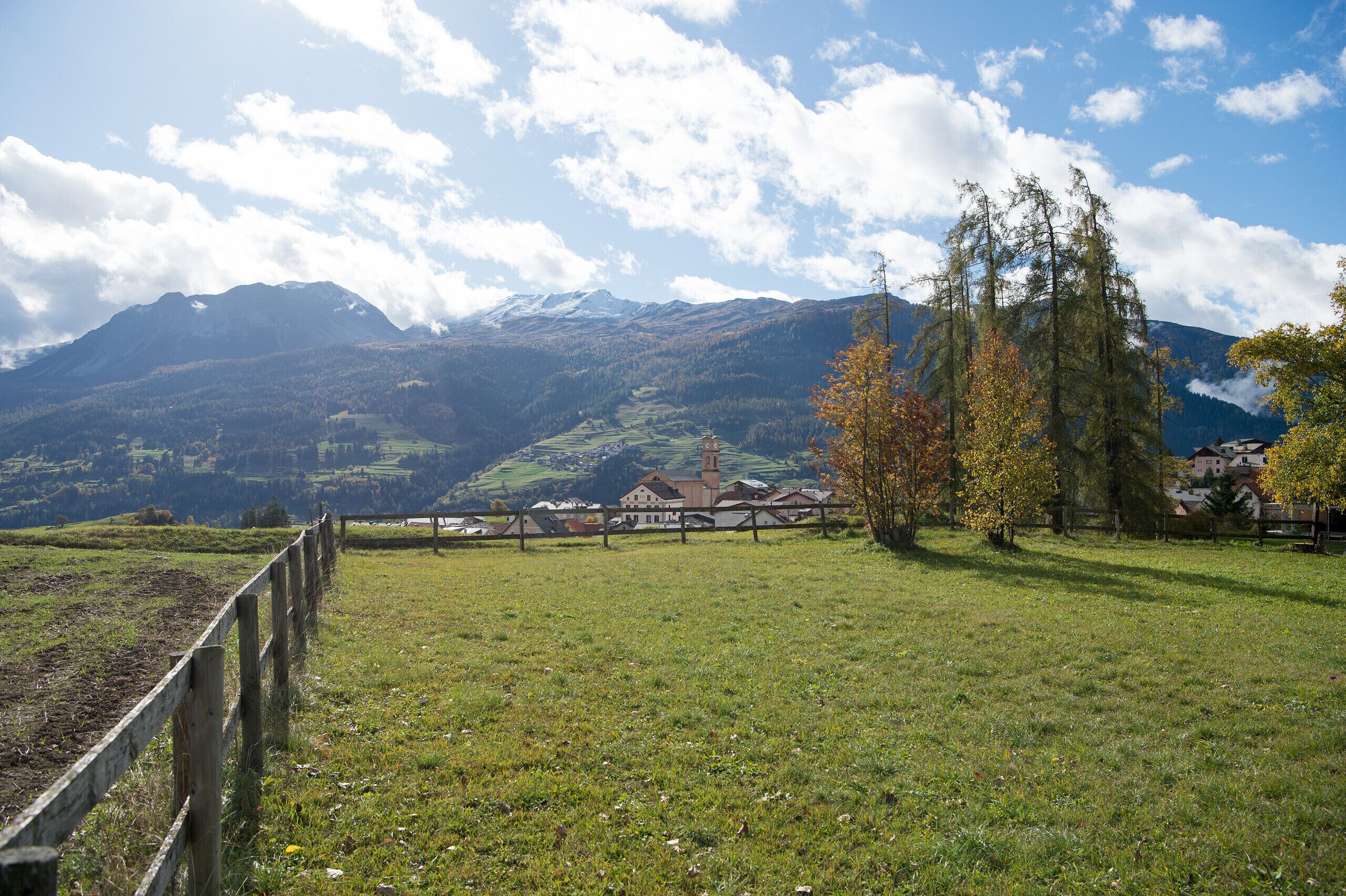 Un paysage rural avec une clôture en bois, un ciel dégagé et des montagnes à l’horizon.