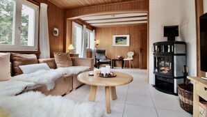 A cozy living room with a wooden ceiling, a sofa with a fur throw, a round wooden coffee table, and a fireplace.