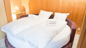 A large bed with white linens and pillows, a wooden headboard, and a bedside table with a lamp.