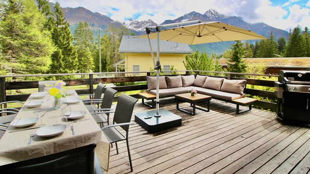 A deck with a dining table set for six, a sofa, and a grill.