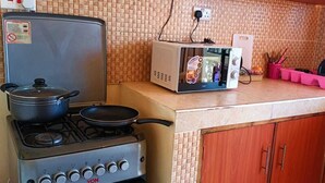 A kitchen with a gas stove, a microwave, and a small refrigerator. There are cabinets and a countertop with dishes and utensils.