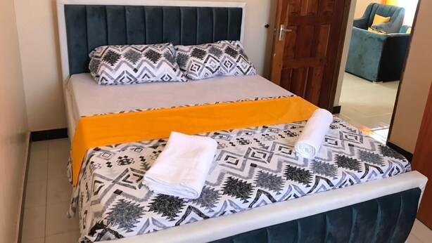 A bed with a patterned bedspread, a white pillow, and a folded towel.