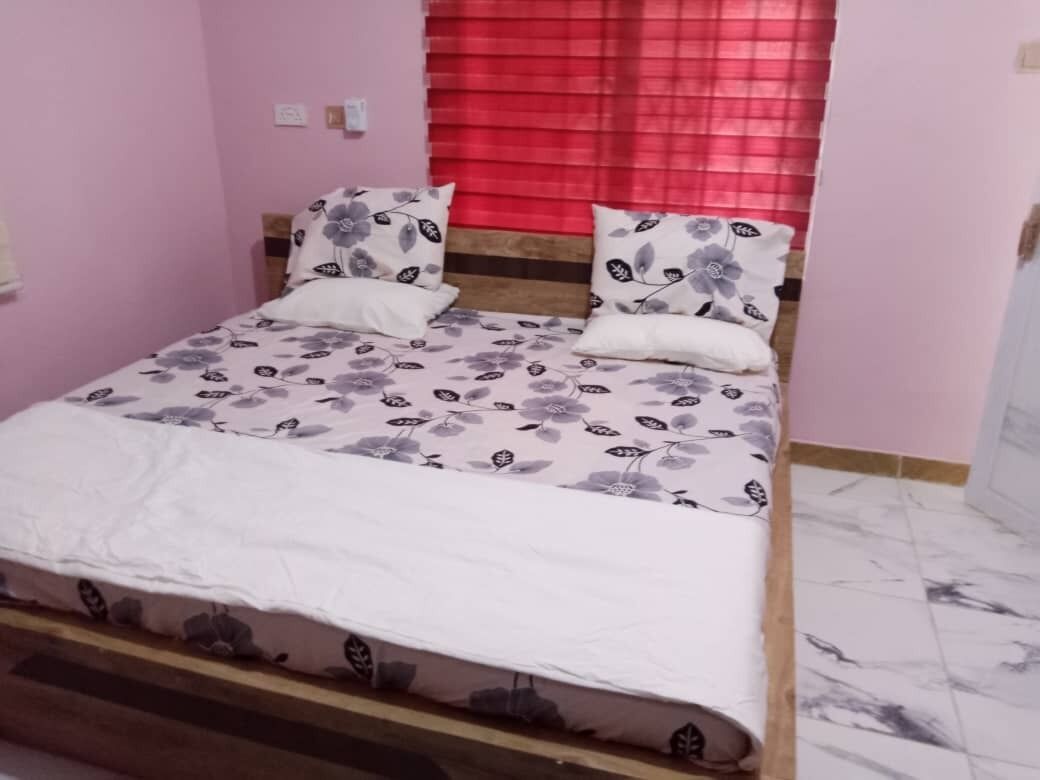 A bed with floral bedding, a wooden headboard, and a red window blind.