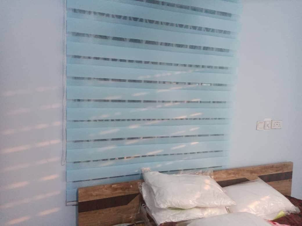 Una habitación con una cama, cabecera de madera y ventana con persianas horizontales.