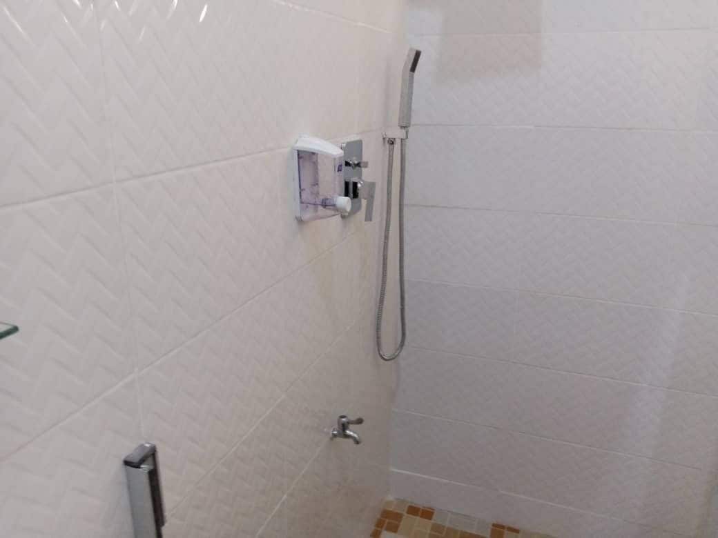 Un petit espace de douche fermé, équipé d’un pommeau de douche à main et d’un boîtier de commande fixé au mur.
