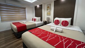 A hotel room with two beds, each with red and white bedding, a large window with blinds, a ceiling light, and a wall-mounted air conditioner. - Khotel near T3 Airport (Pasay)
