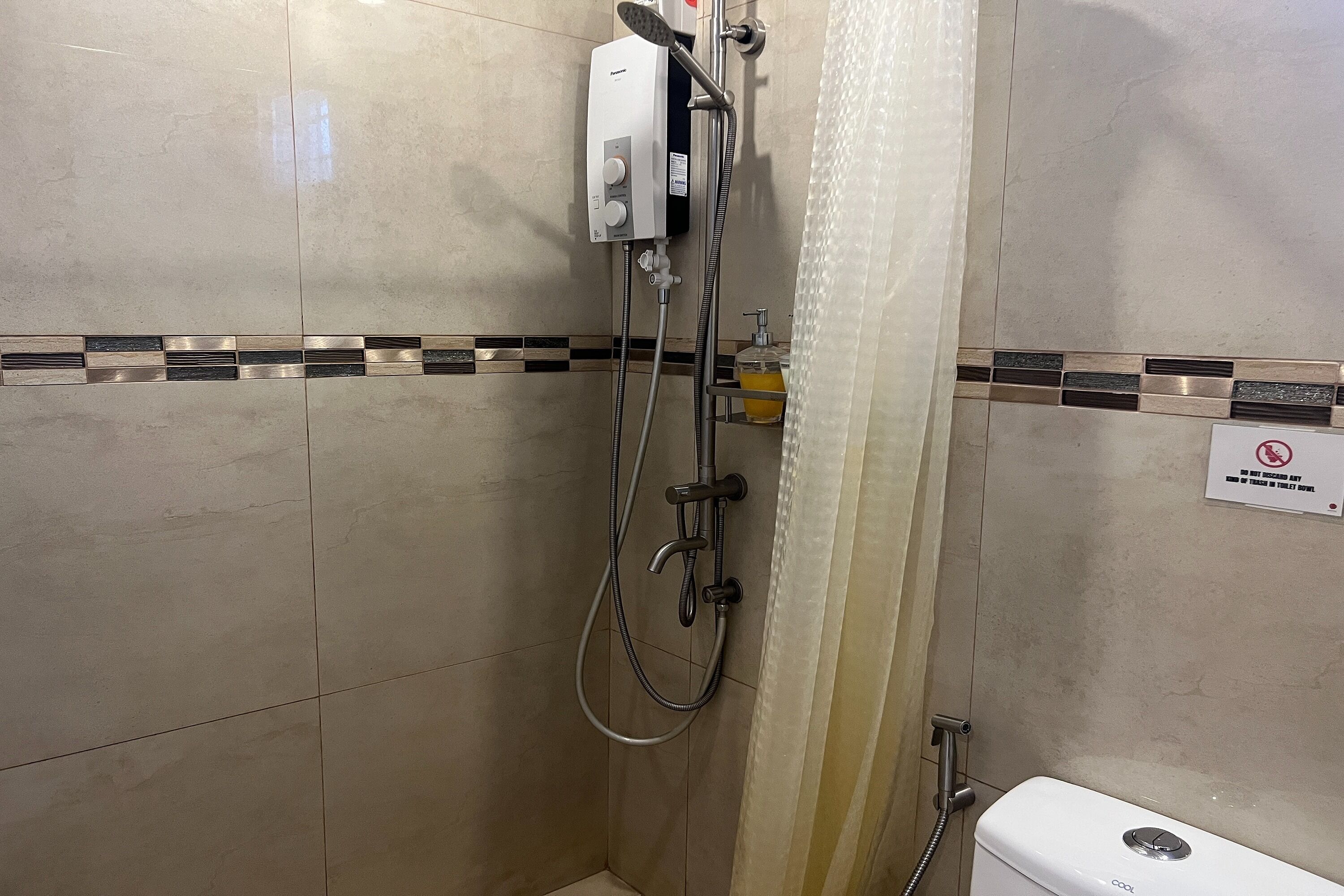 A shower area with a handheld showerhead, a wall-mounted control panel, and a no-smoking sign.