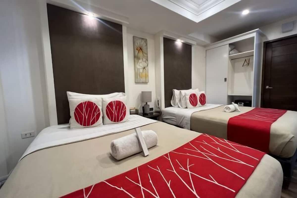 A hotel room with two beds, a mirror, a nightstand, and a ceiling light.