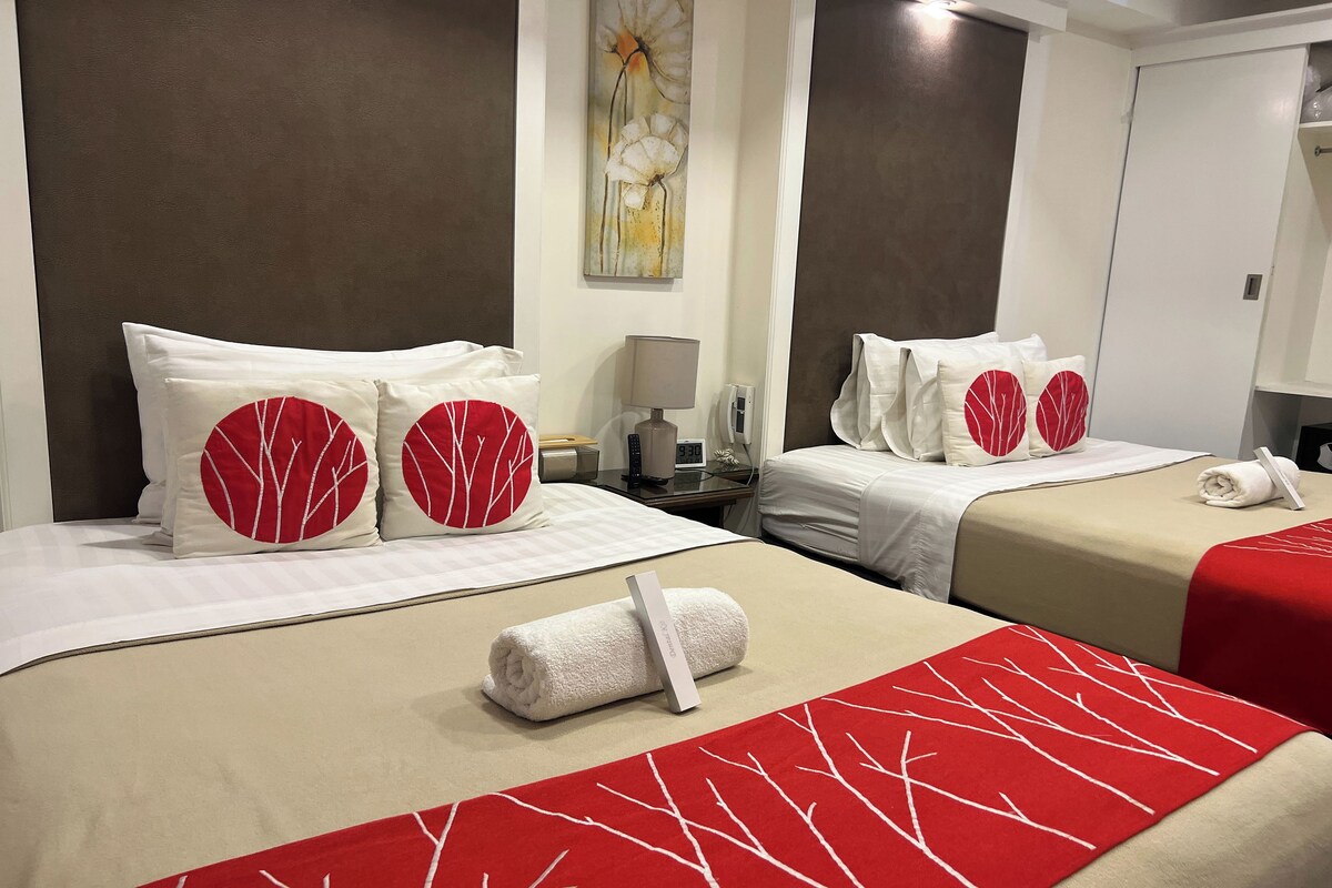 A hotel room with two beds, each with red and white bedding, a wall clock, and a painting.