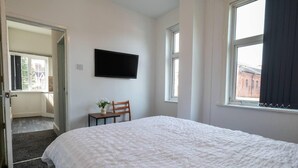 A bedroom with a large bed, a flat-screen TV mounted on the wall, and a chair with a small table and flowers. - Impeccable Flat 1-bed Studio12 in Coventry (Coventry)
