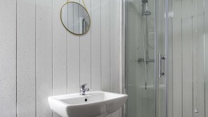 Een badkamer met een witte wastafel, een ronde spiegel en een douche met glazen wanden.