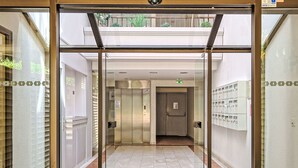 Une entrée d’ascenseur avec une porte en verre, un panneau indiquant clairement la sortie de secours et un sol carrelé.