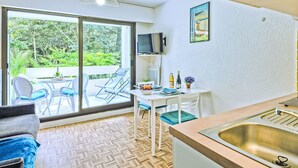 Une cuisine compacte comprenant un évier, un coin repas avec des chaises et une table, ainsi qu’une porte-fenêtre coulissante donnant sur un espace extérieur aménagé avec vue sur la verdure.
