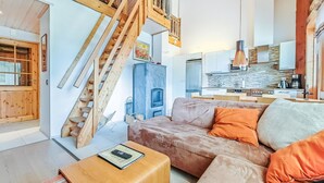 Un salon moderne avec un canapé, une table basse et une cheminée. Un escalier en bois mène à l’étage supérieur.