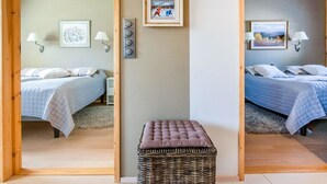 Une chambre avec deux lits, chacun recouvert d’une courtepointe bleue matelassée, un petit pouf en osier et des lampes fixées au mur. Des tableaux encadrés ornent les murs.