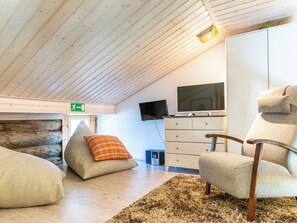 Een gezellige kamer met een schuine kap, een flatscreen televisie, een witte dressoir, een comfortabele stoel en een zacht tapijt.