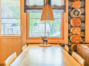 Un comedor con una mesa y sillas de madera, una lámpara decorativa y vistas al exterior a través de amplios ventanales.