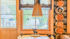 Un coin repas comprenant une table en bois, des chaises, une sculpture décorative représentant un cerf, une lampe suspendue et une fenêtre avec des stores.