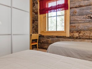 Quarto com parede de madeira, janela com persianas, uma cadeira e uma cama.