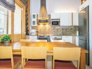 Una cocina moderna con una mesa de comedor de madera, sillas, una lámpara colgante y electrodomésticos integrados.