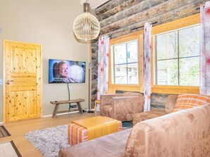 Een gezellige woonkamer met een televisie, houten meubels en grote ramen.