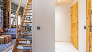 A modern interior with a wooden staircase leading to a loft area, a cozy seating area with a sofa and cushions, and a large wooden door.