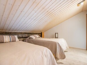 Una habitación con dos camas, listones de madera en el techo y una pared de piedra.