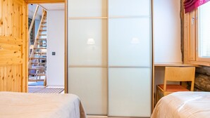 A room with two beds, a wooden wardrobe, a sliding glass door, a small table, and a window with curtains.