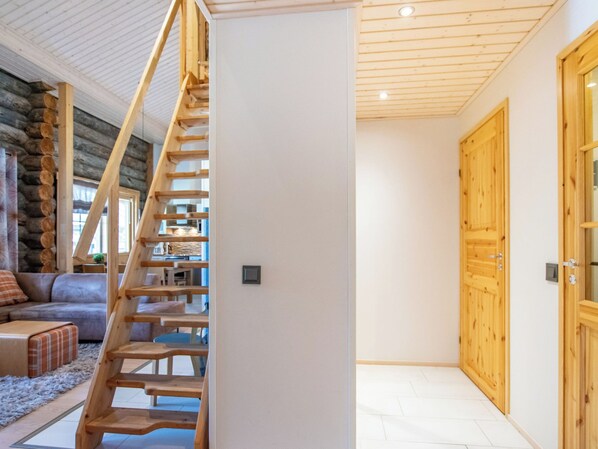 A modern interior with a wooden staircase leading to a loft area, a stone wall, and a large wooden door.