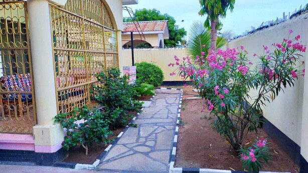 Un patio con un camino de piedra, una reja de metal y plantas con flores.
