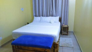 Habitación con una cama individual, cabecera de madera, mesita de noche pequeña y un banco azul al frente.