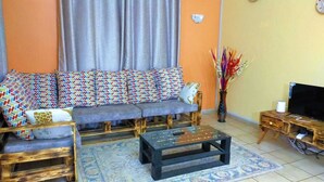Una sala de estar con un conjunto de sofás, una mesa de centro, un mueble para televisor y un jarrón decorativo.