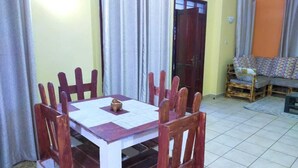 Un comedor con mesa y sillas de madera, una lámpara de mesa pequeña, y una puerta que da a otra habitación.