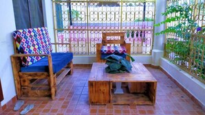 Un pequeño balcón con un banco de madera, una mesa de madera y una silla con un cojín colorido.