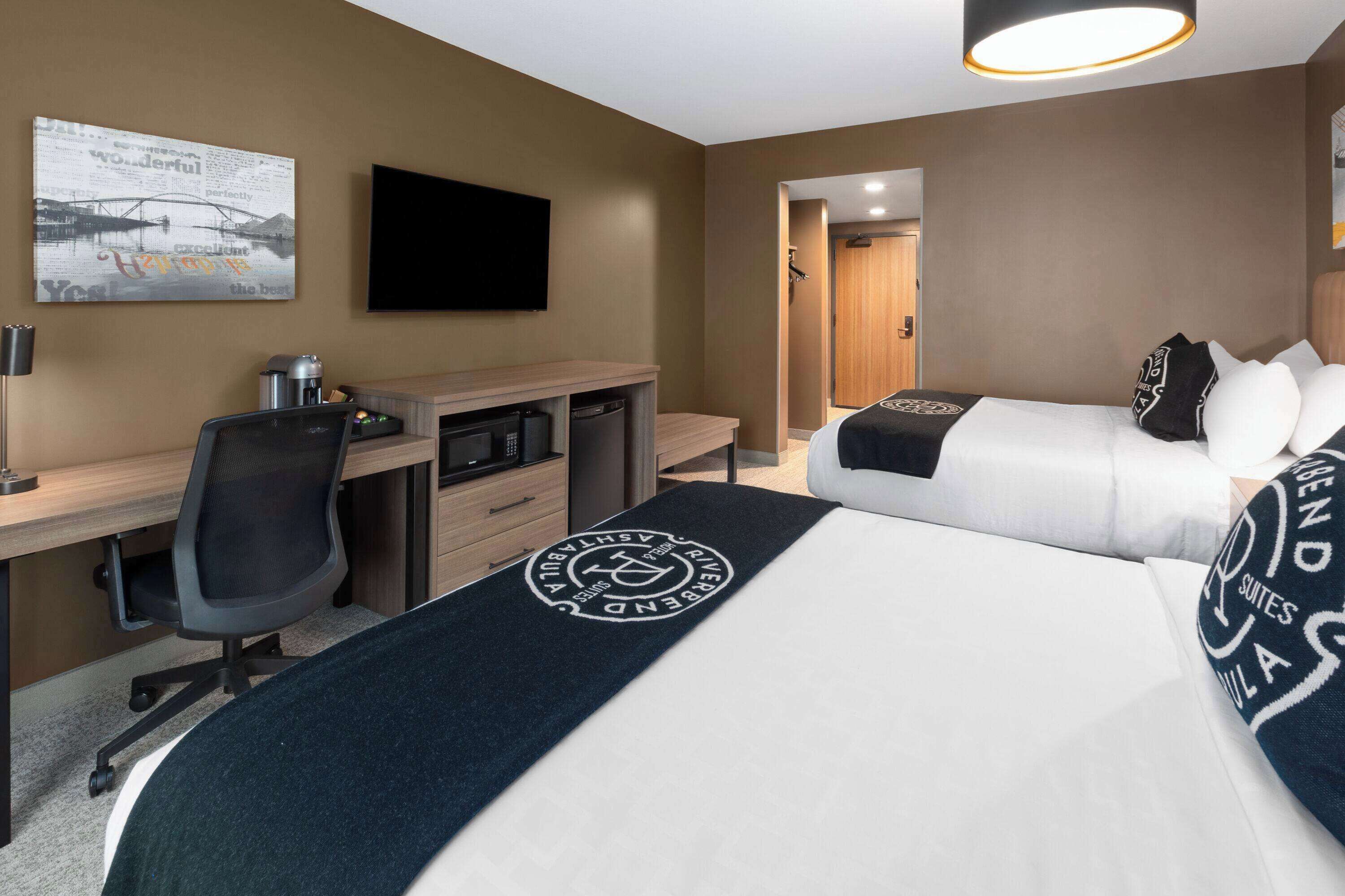 A hotel room with a bed, a desk, a chair, a TV, and a bathroom door.